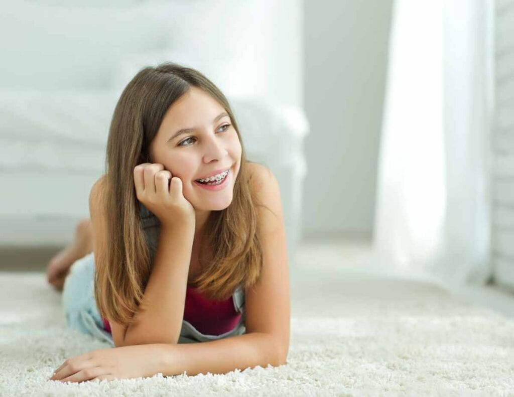 Teenager with braces for teens laying on he front on soft white carpet