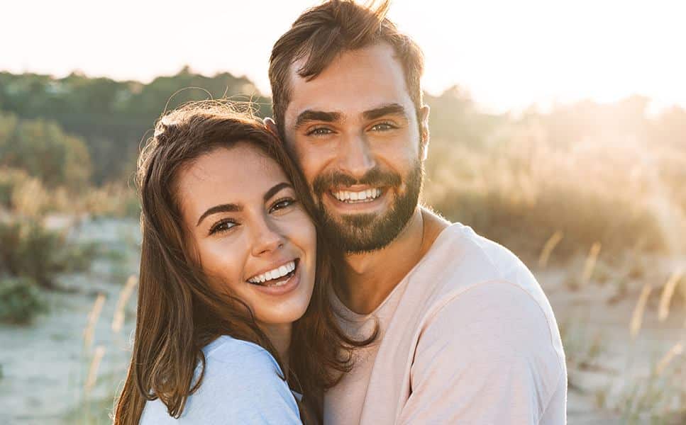 Adult couple with Invisalign for adults smiling together in an evening sunset