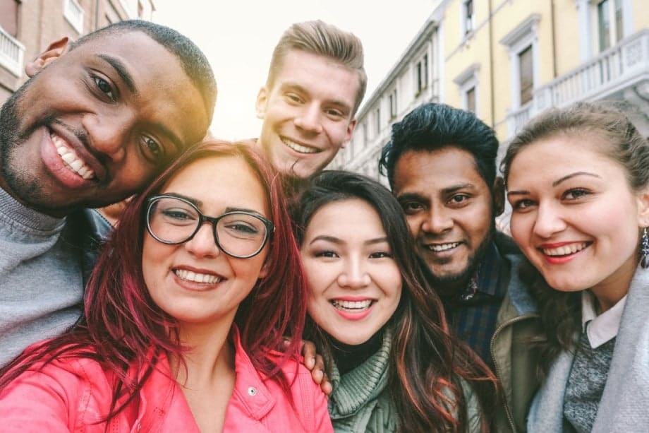 Diverse group of women and men huddled together for a selfie on a small street at sunset