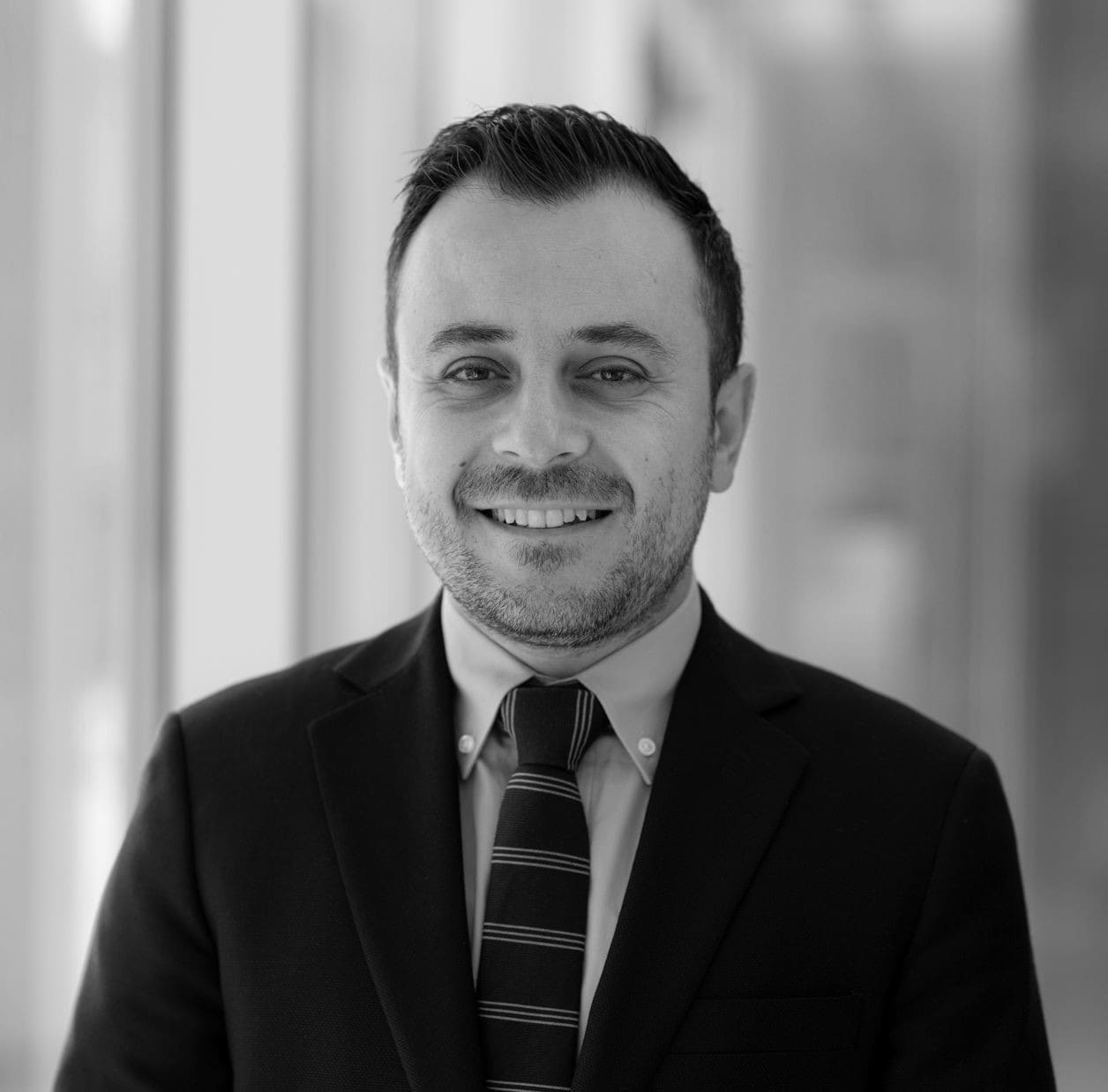 Black and white headshot of orthodontist Dr. Ankah smiling in a suit and tie