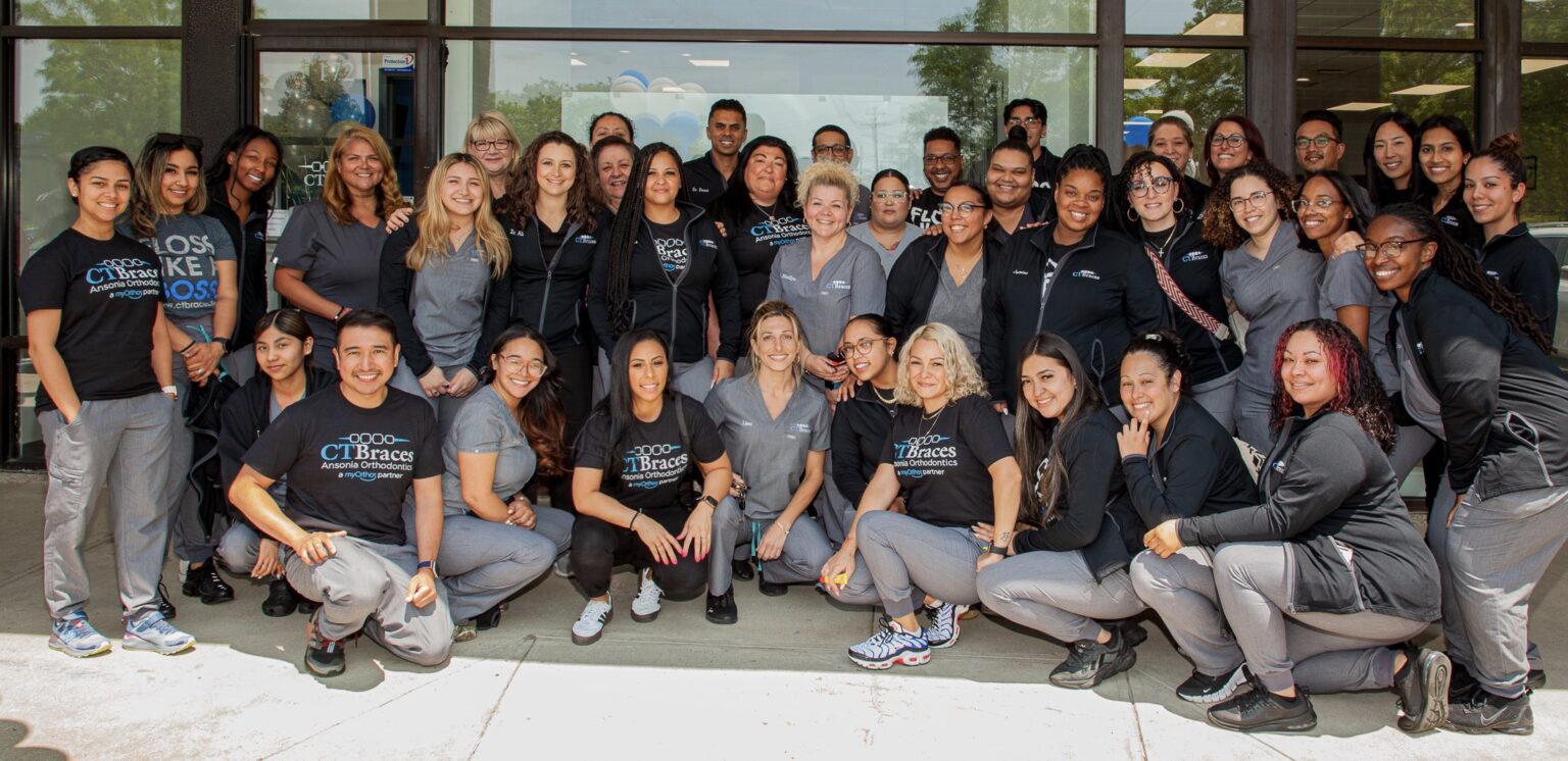 Panorama of CT Braces team posing in a large group in front of the office.