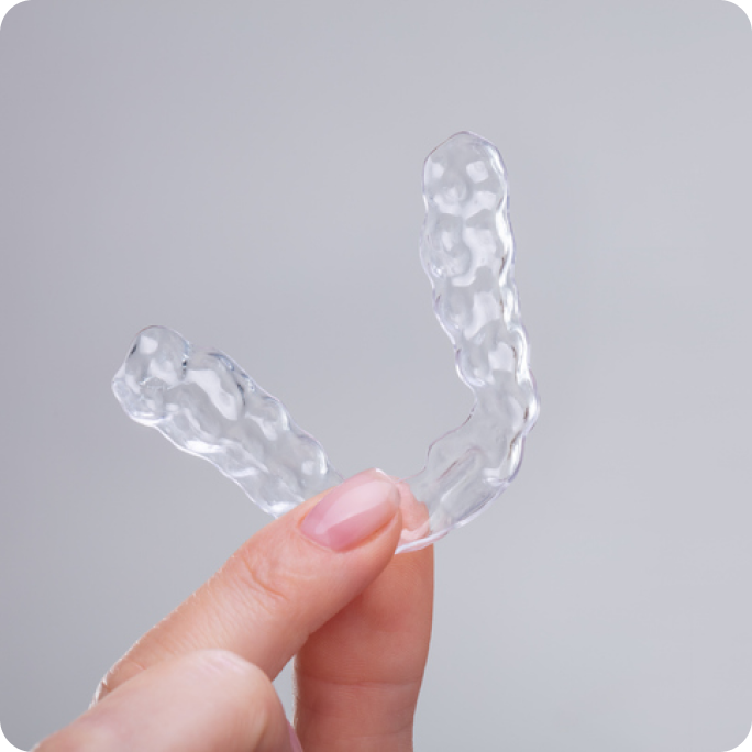 Close up of an Invisalign clear aligner being held between someone’s thumb and index finger