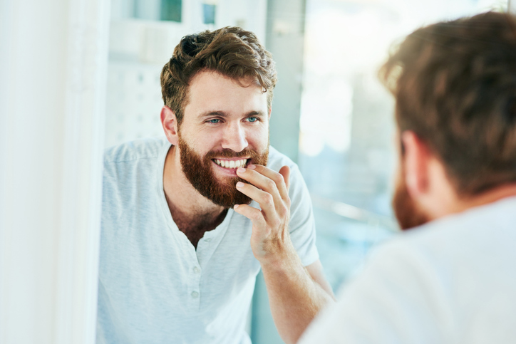 A man looking at his teeth in the bathroom mirror.