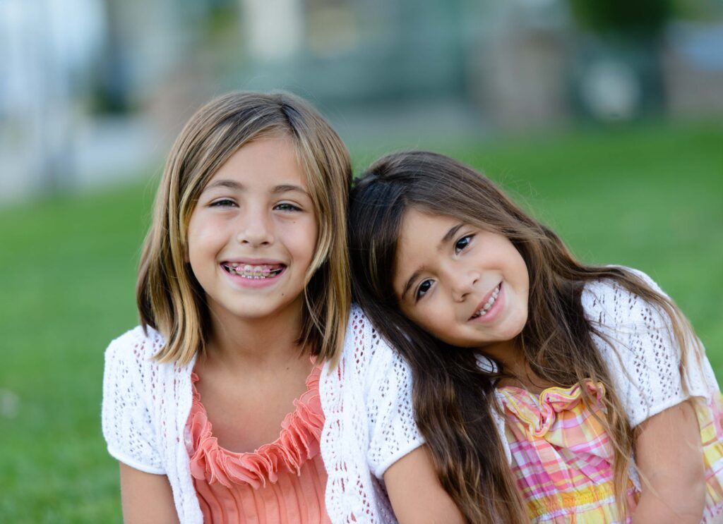 2 girls undergoing early orthodontic treatment in New Haven, CT smiling in a field