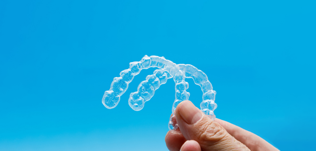 Close up of Invisalign® in New Haven, CT being held up in front of a blue background