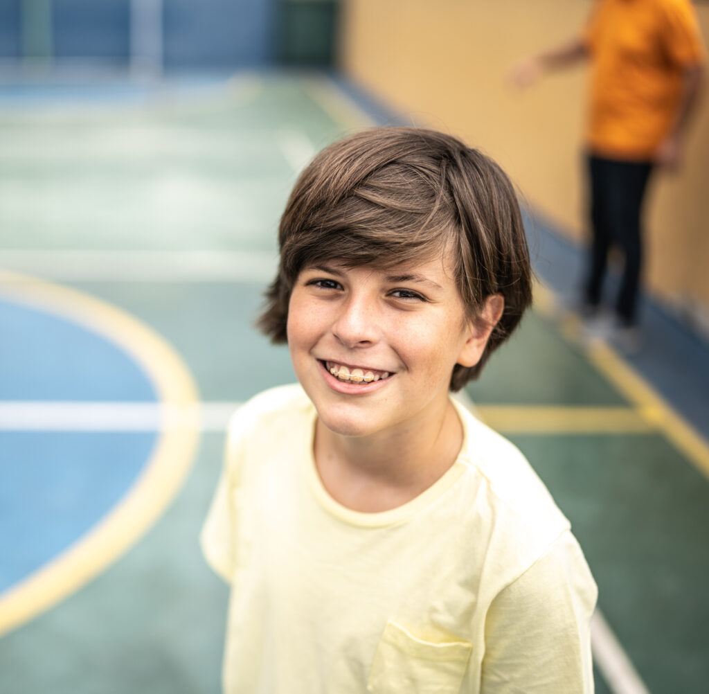 Boy who is undergoing early orthodontic treatment in Danbury, CT smiling on a basketball court