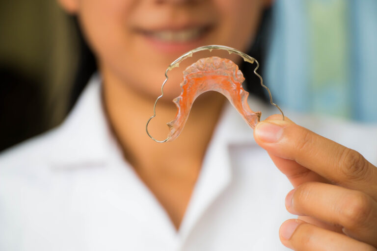 Orthodontic assistant in white holding a removable retainer