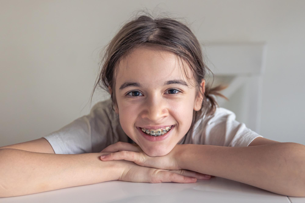 Girl undergoing early orthodontic treatment in Orange with braces for kids smiling at a desk