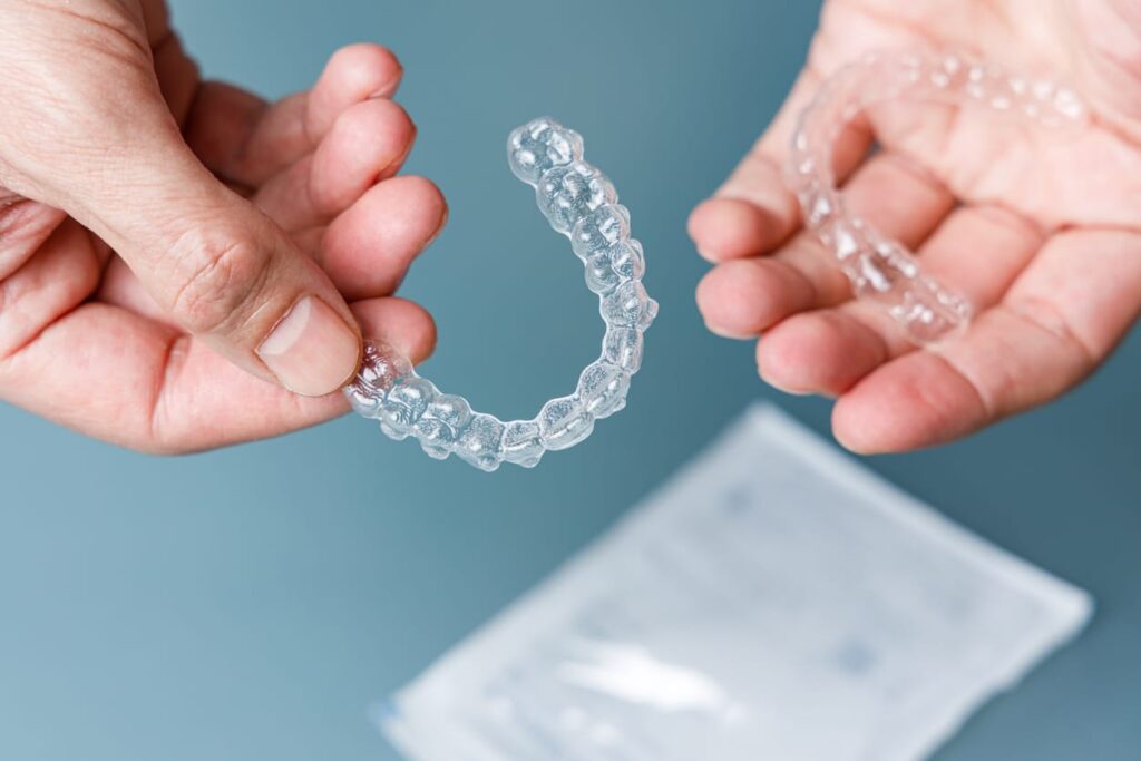 Person with Invisalign® in Orange, CT holding one of their aligners in each hand